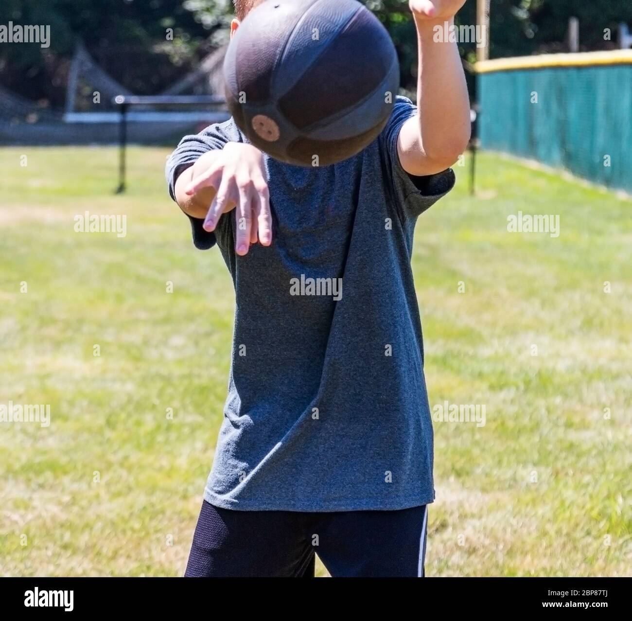 Atleta adolescente che lancia una palla medica alla telecamera in piedi su un campo di erba. Foto Stock