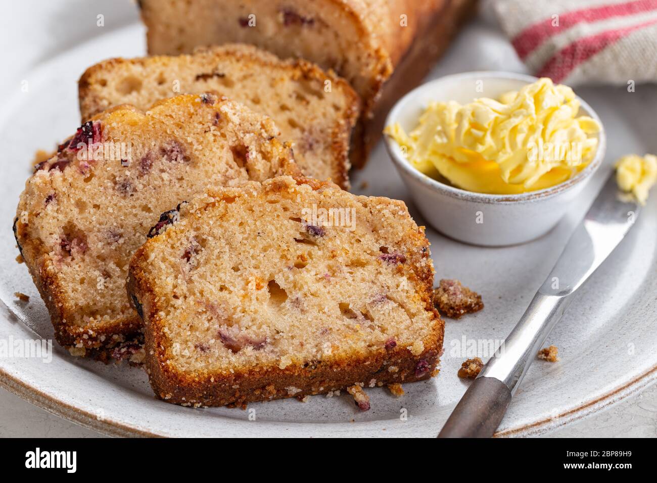 Primo piano di torta di pane di arancio al mirtillo e ciotola di burro su un piatto Foto Stock