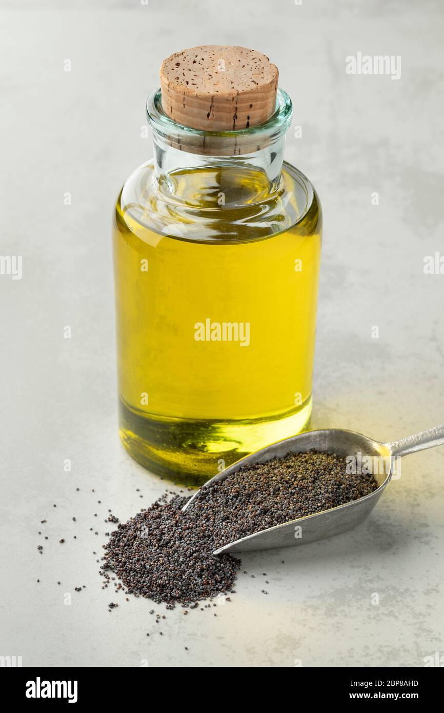 Bottiglia con olio di semi di papavero nero e un cucchiaio con semi di papavero Foto Stock