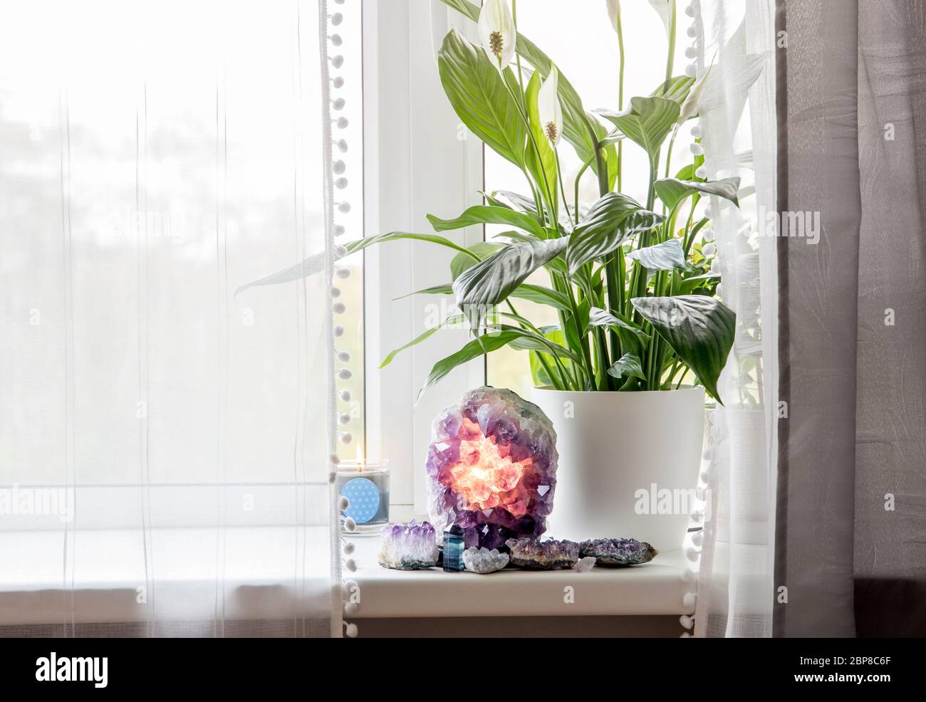 Utilizzando dettagli in cristallo di pietra semi-preziosi in concetto domestico. Lampada geode ametista bruciante, atmosfera spirituale calmante casa. Impianto pneumatico Spathiphyllum. Foto Stock