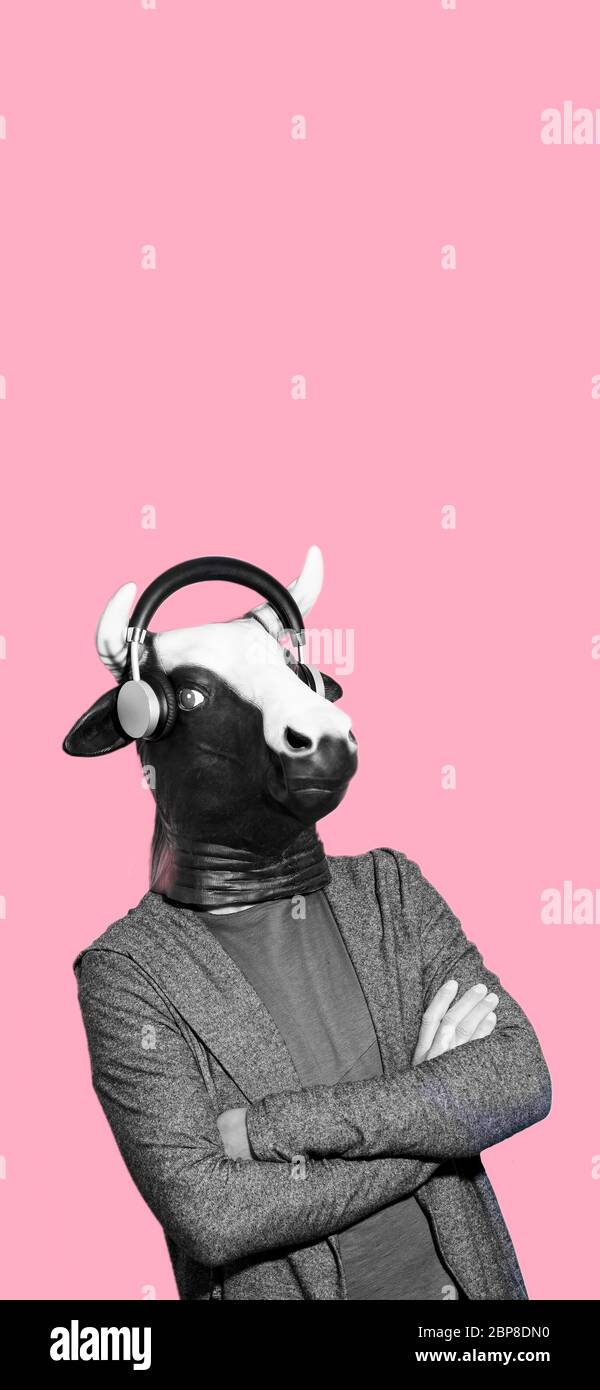 ritratto di giovane uomo che indossa una maschera di mucca e auricolari in bianco e nero su uno sfondo rosa con un po 'di spazio vuoto sulla parte superiore, in un formato verticale a u Foto Stock