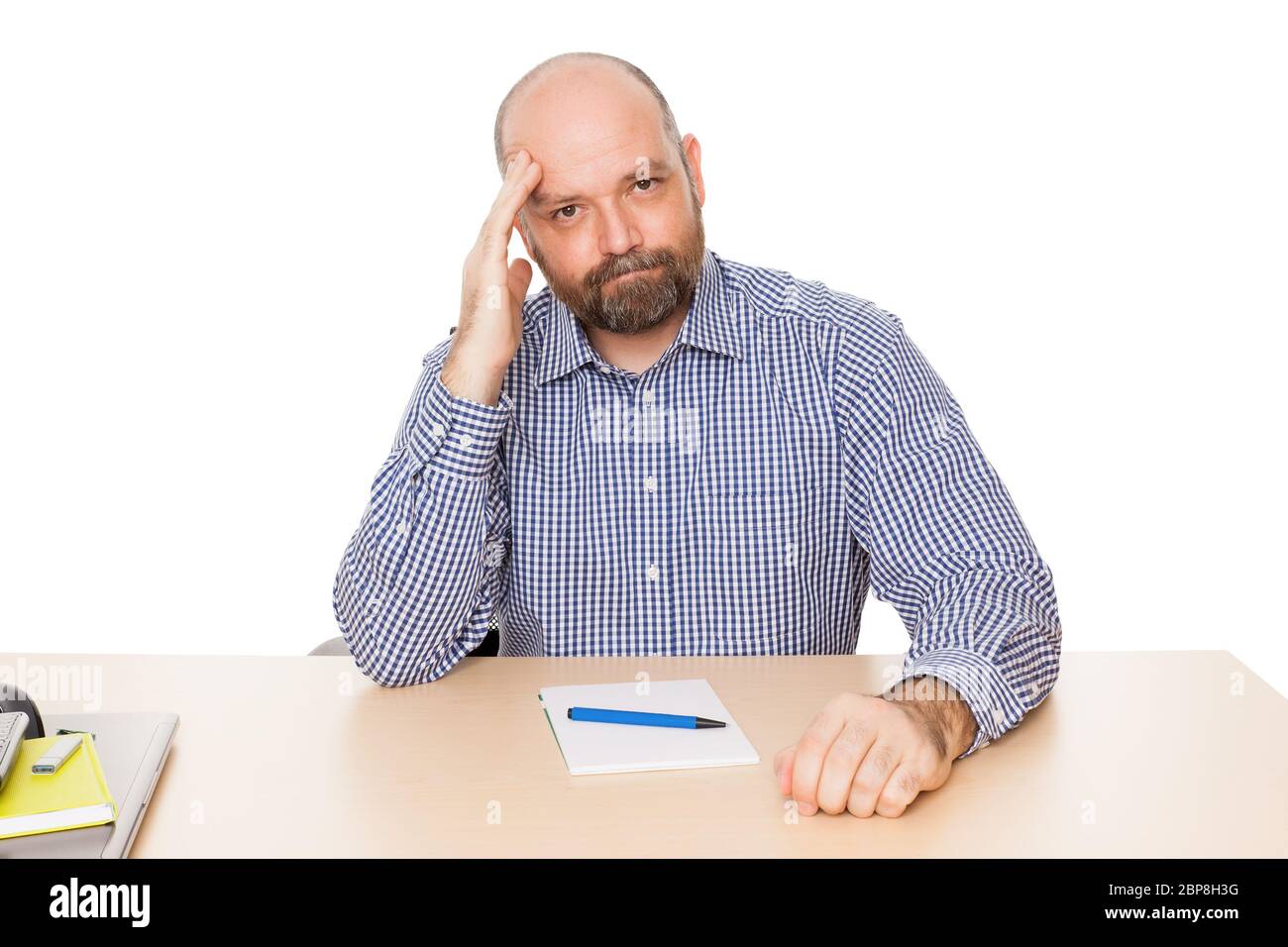 Ein ratloser Mann mit Bart un seinem Schreibtisch vor weissem Hintergrund Foto Stock