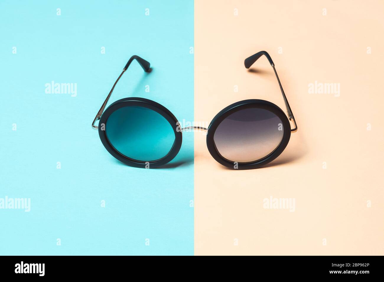 Foto di moda, occhiali da sole rotondi su sfondo blu pastello e corallo. Concetto estivo minimo. Foto Stock