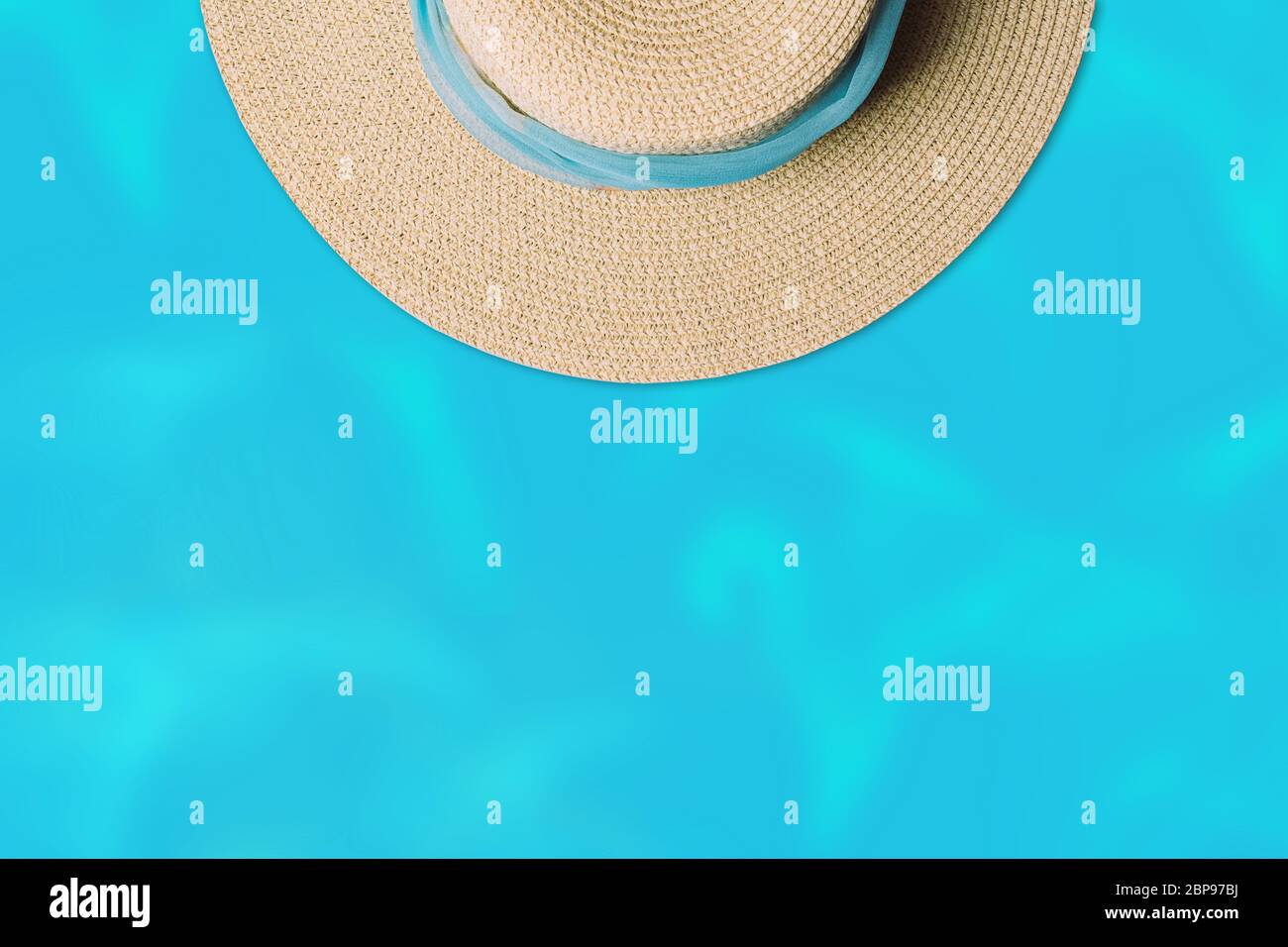 Vista dall'alto sul cappello da spiaggia in paglia con sciarpa blu sullo sfondo dell'acqua. Concetto estivo minimo con spazio di copia. Foto Stock
