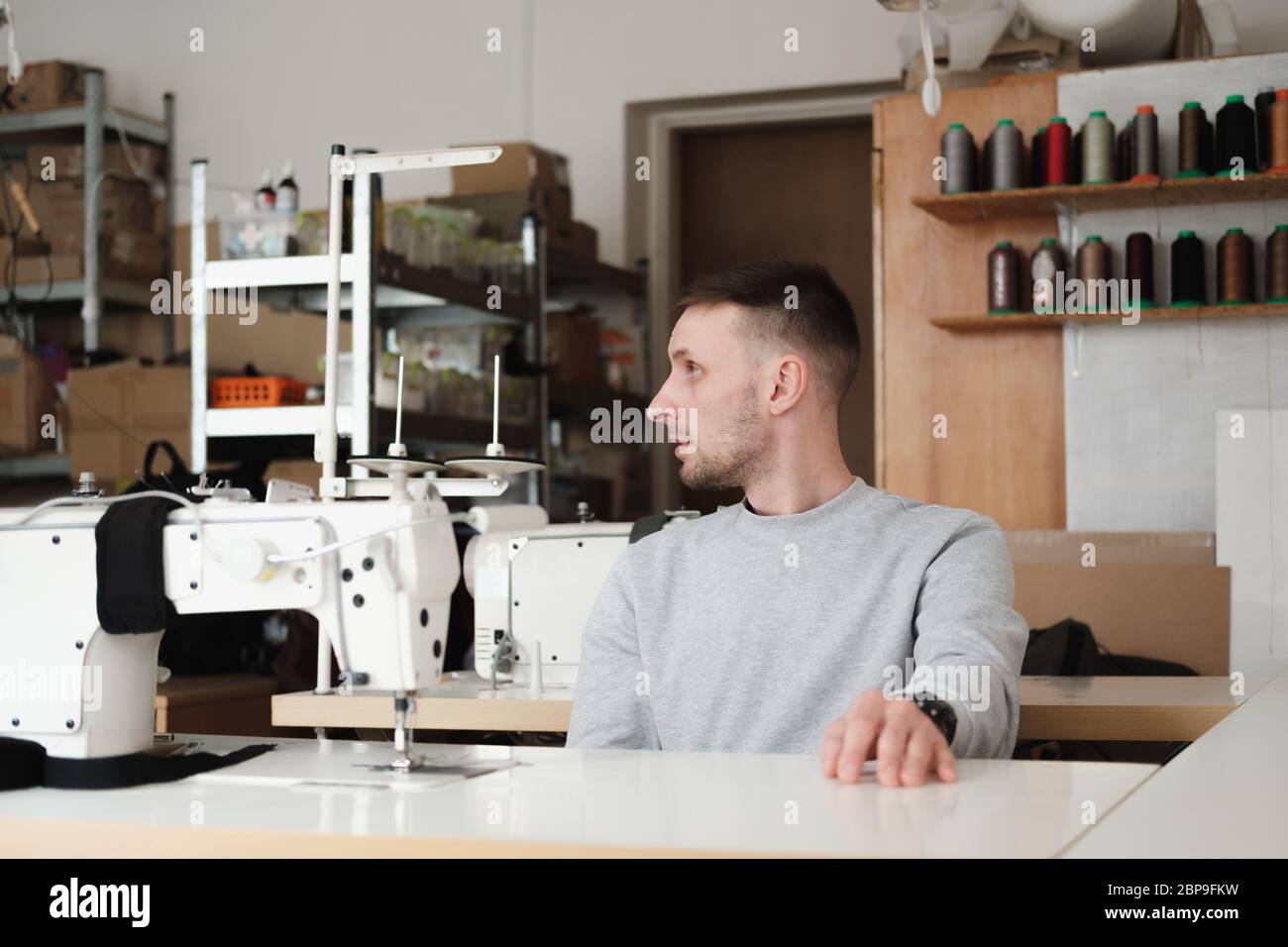 Proprietario di un'azienda locale su misura o di piccole dimensioni in un'officina generica. Uomo seduto davanti alla macchina da cucire, luce naturale Foto Stock