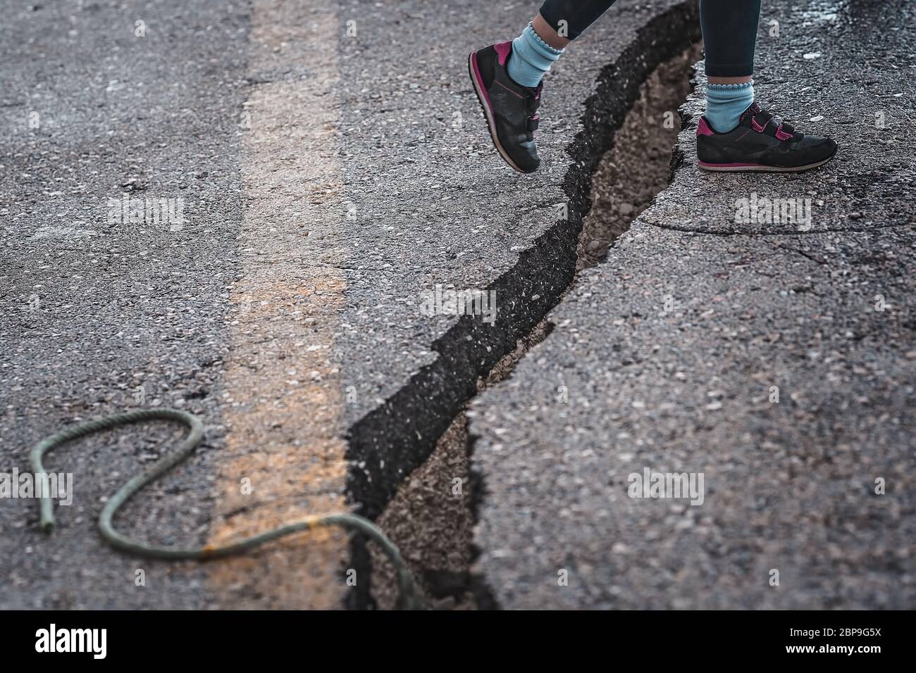 Bambina saltando il crack gap in strada in città in estate Foto Stock