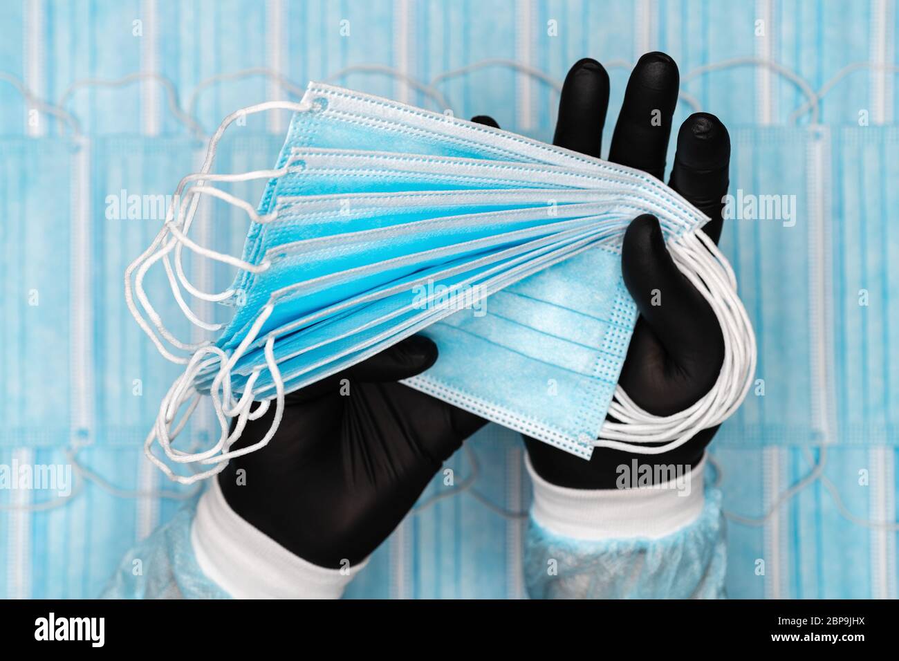 L'uomo medico tiene molto blu maschere respiratorie chirurgiche in guanto protettivo nero in due mani. Immagine concettuale sulle bende respiratori di sfondo Foto Stock