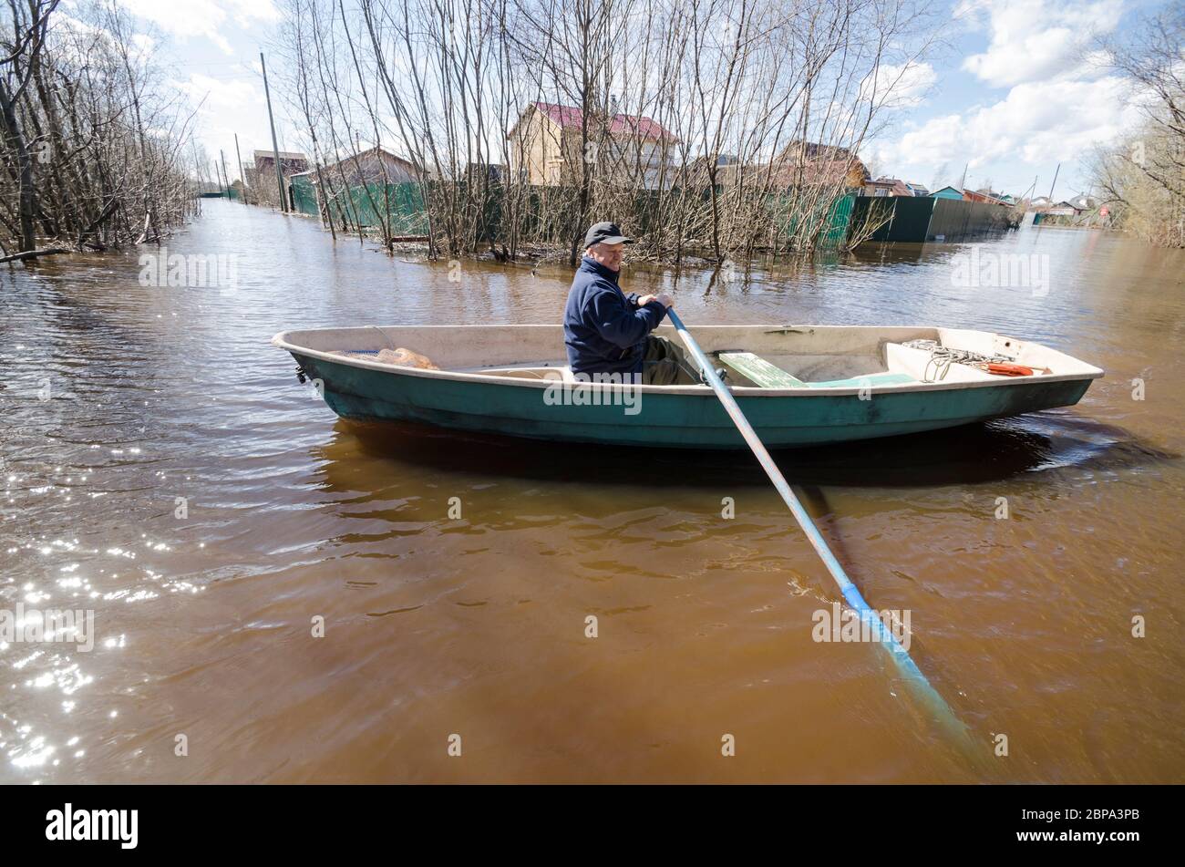 Un anziano guida una barca lungo una strada allagata. Alluvione Foto Stock