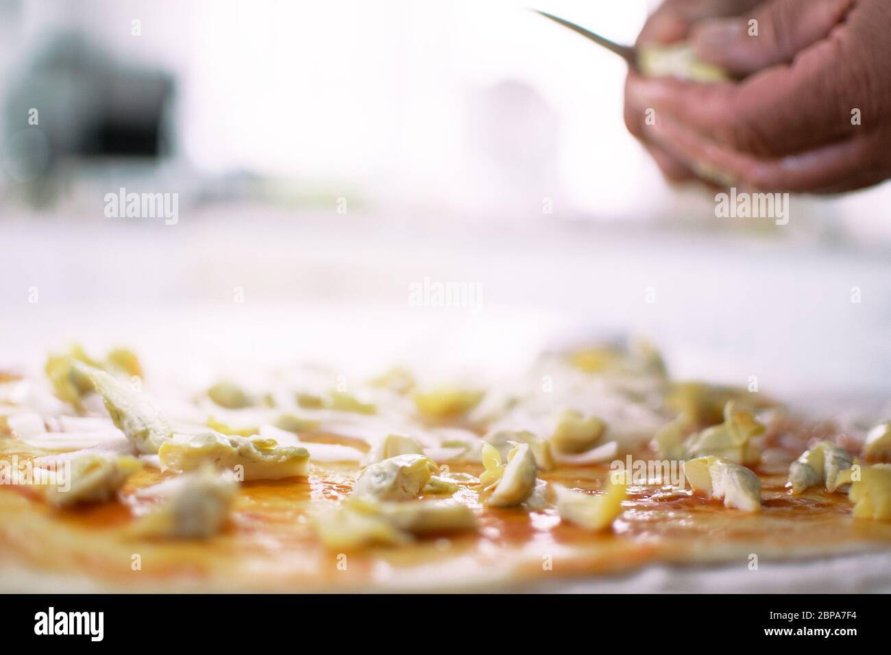 Cucina tradizionale della pizza da chef italiano a casa. Aggiungere i pezzi di carciofo. Aggiungere gli ingredienti sopra. Semplice ma delizioso tradizionale italiano m Foto Stock