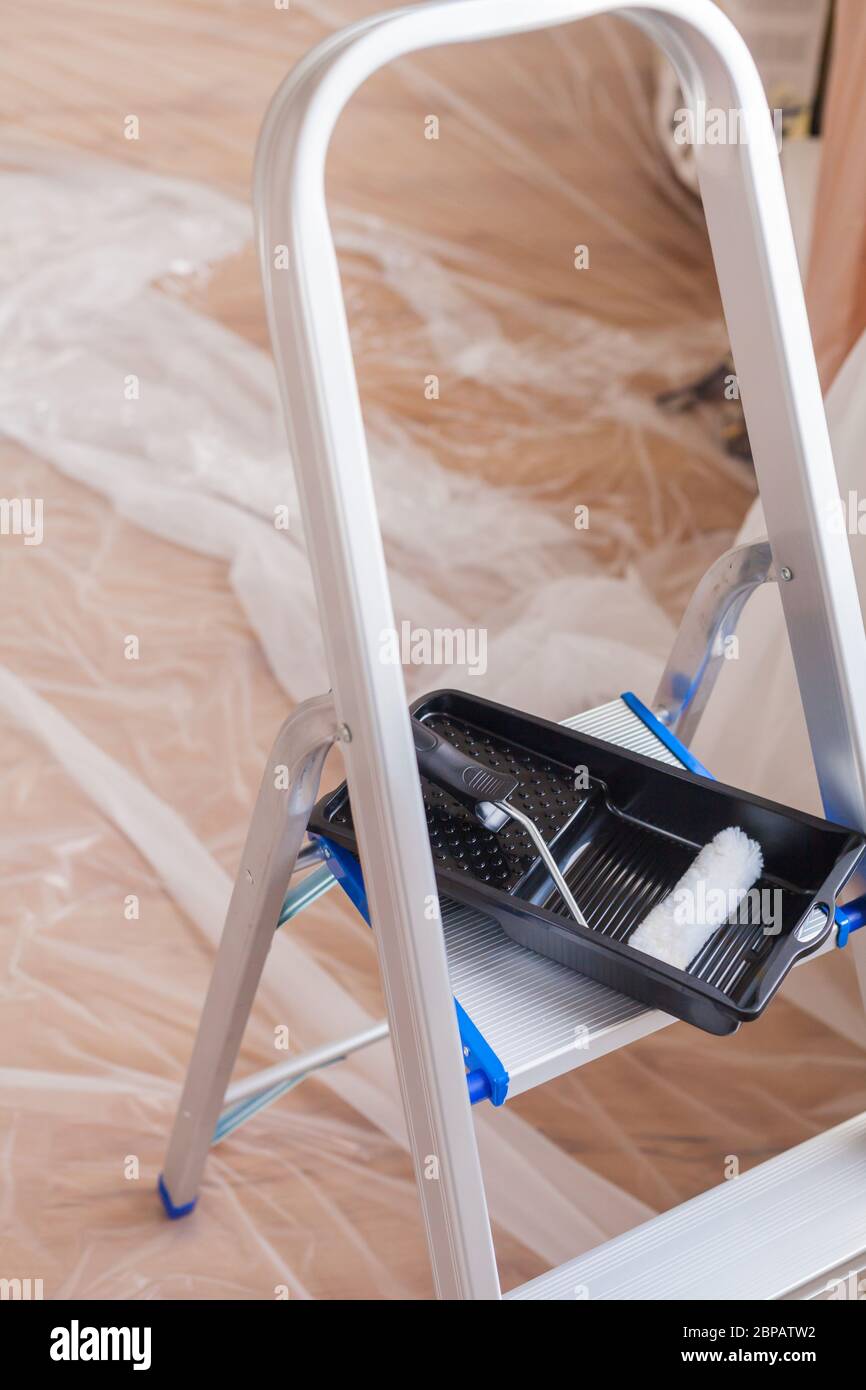 Scala in alluminio è ripiegata sul pavimento con nastro adesivo con vassoio antigoccia preparazione vernice di ristrutturazione artigianale fare da soli gli attrezzi Foto Stock