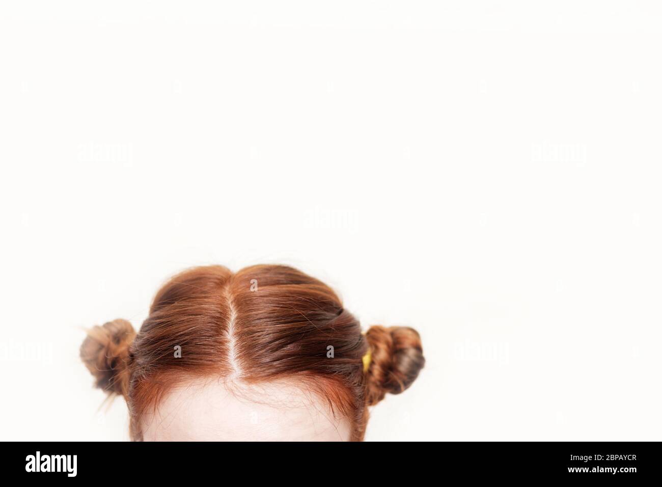 Testa di una ragazza con due grappoli di capelli rossi ricurci e intrecciati su sfondo bianco. Capelli creativi. CopySpace Foto Stock