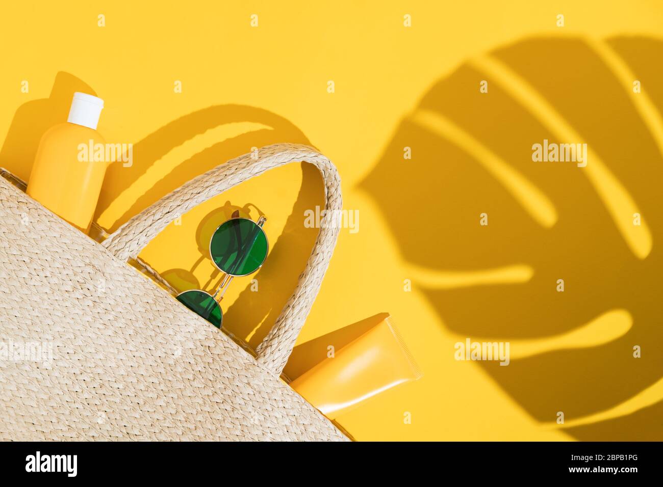 Estate luminoso flatlay su sfondo colorato con sacco di paglia in vimini, tubi o bottiglia con crema solare, occhiali da sole e l'ombra da foglia di monstera. Duro Foto Stock