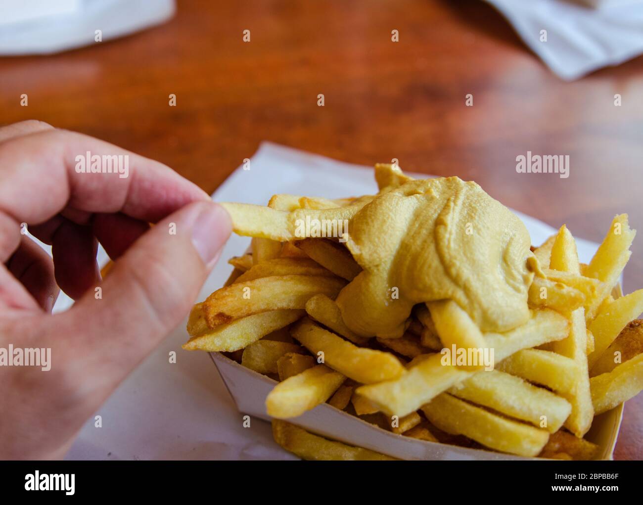 Anversa, Fiandre, Belgio. Agosto 2019. Specialità belga: Patatine fritte guarnite con salsa. La mano immerge un chip di patate nella salsa prima di eatin Foto Stock