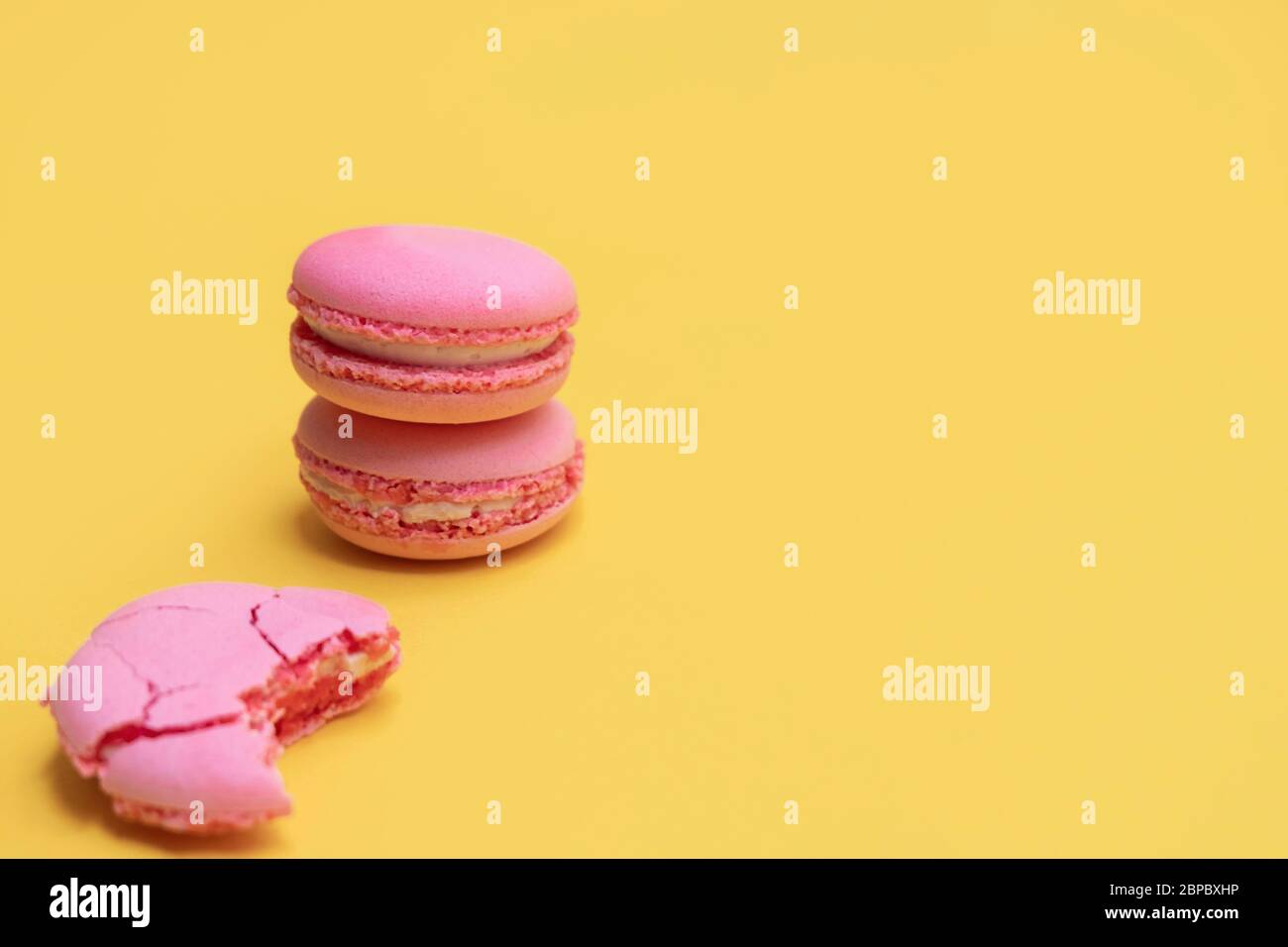 Pila di macaroni rosa su sfondo giallo. Biscotti colorati alle mandorle. Macarons torta pastello sfondo con spazio copia Foto Stock