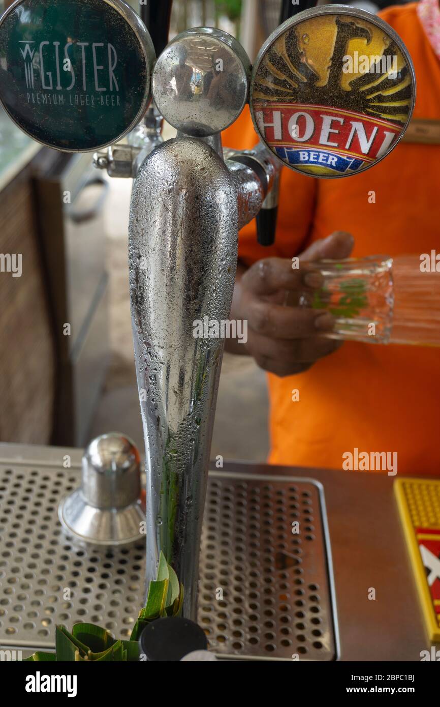 Mauritius, Gennaio 2020 - primo piano rubinetto cromato di un distributore di birra con barista che tiene un bicchiere in un bar sulla spiaggia Foto Stock