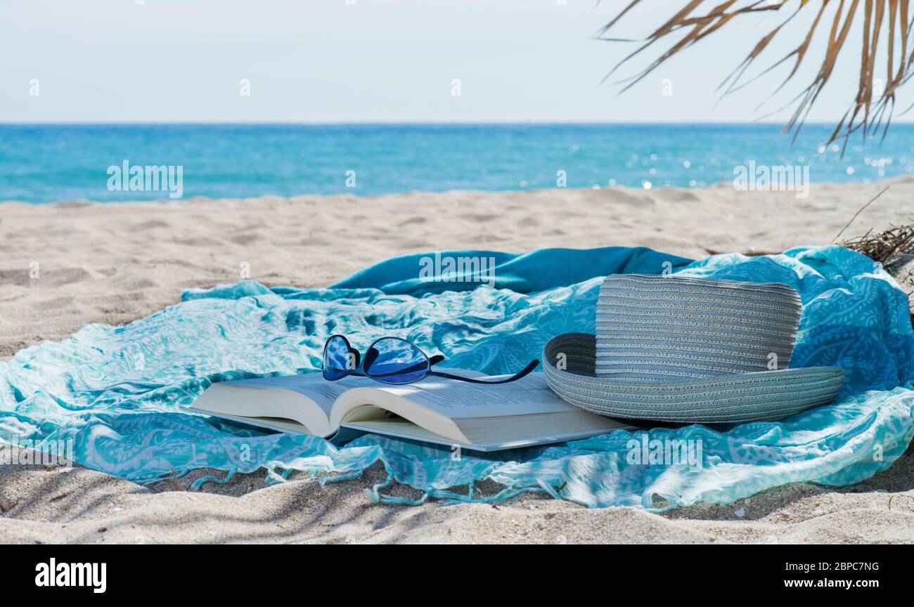 cappello, libro, asciugamano e occhiali da sole sulla spiaggia Foto Stock