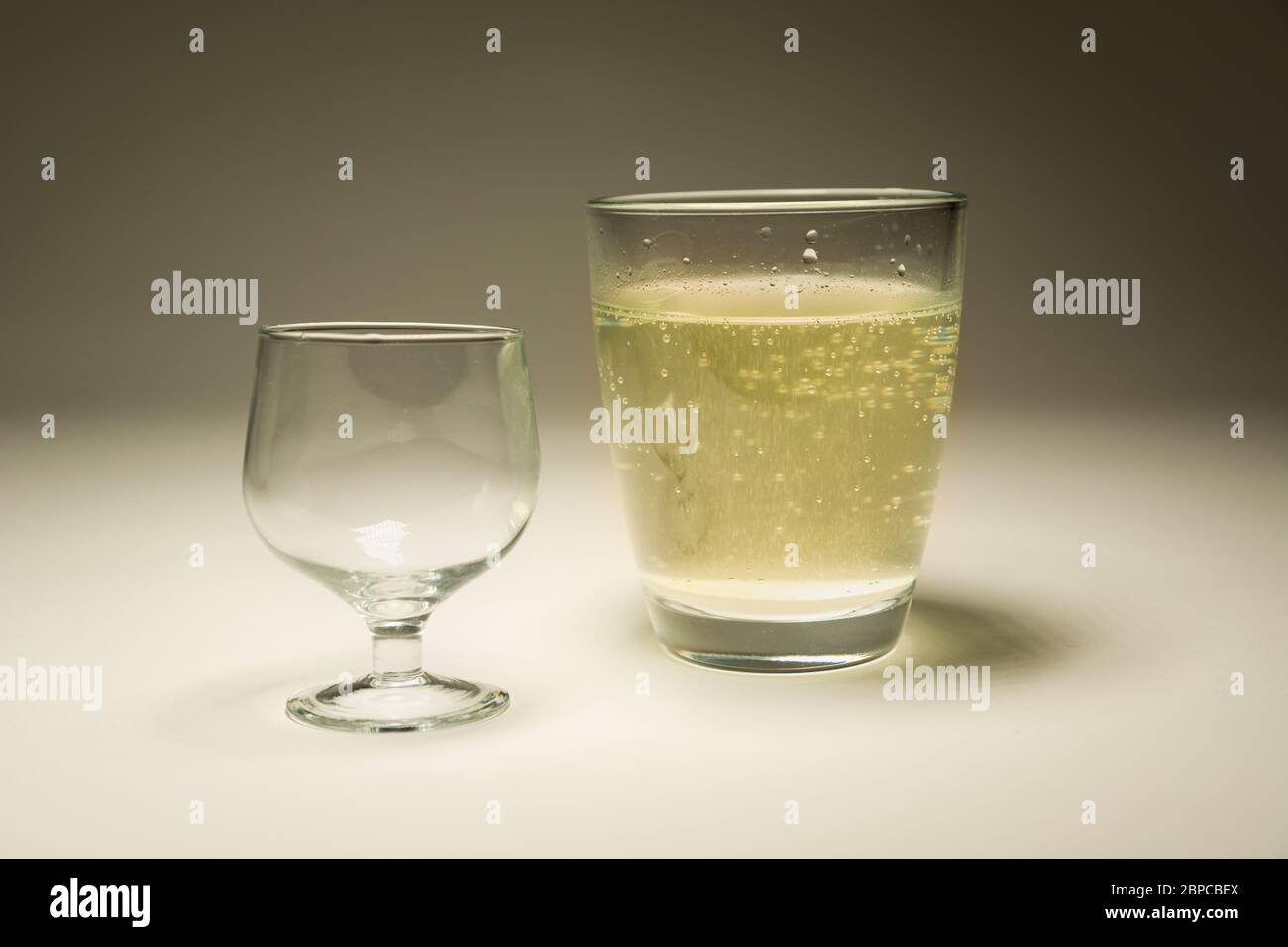 Un bicchiere vuoto e un bicchiere con acqua frizzante, fotografia in studio Foto Stock
