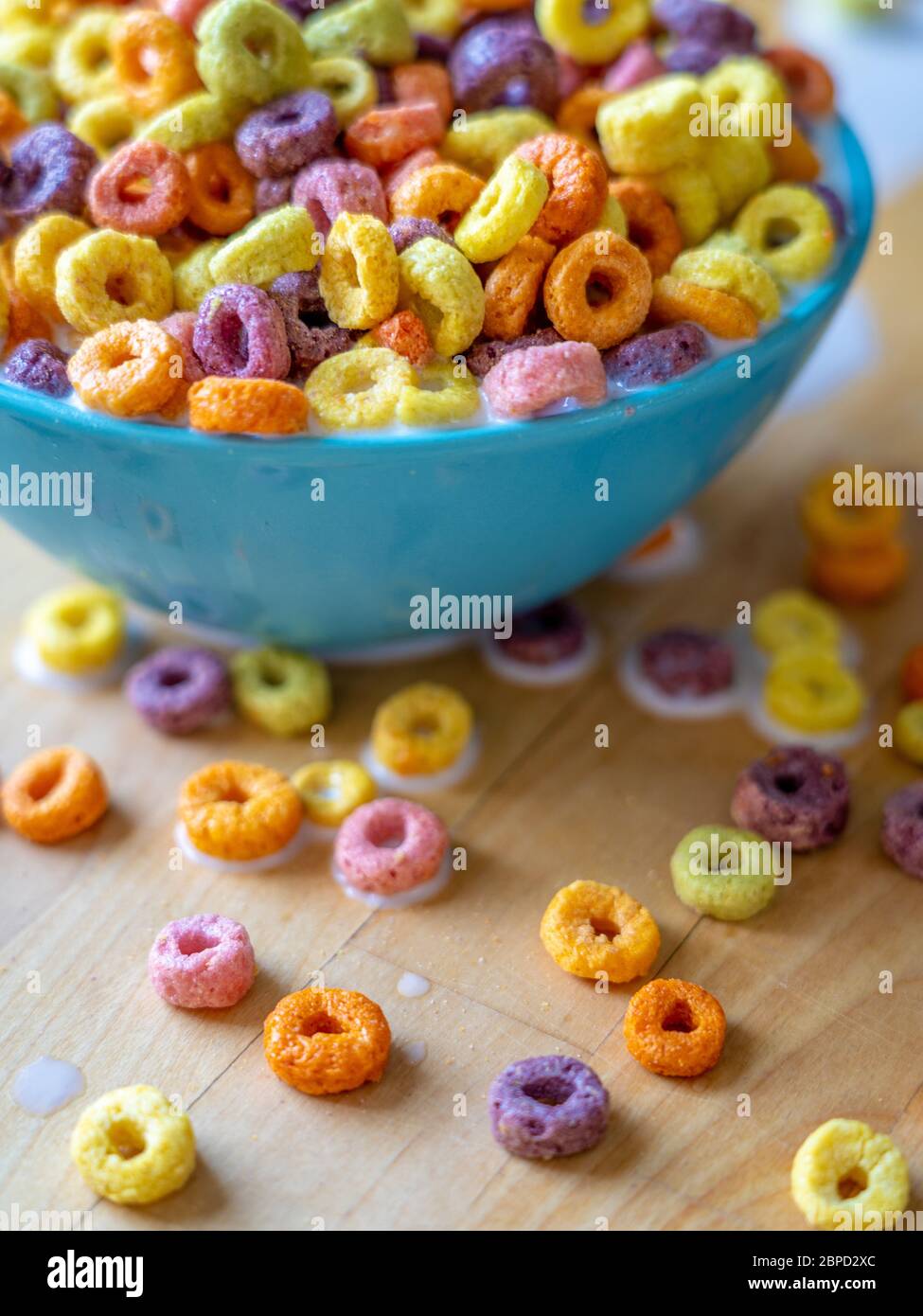 Ciotola colorata di cereali che si versano sul piano del tavolo in legno. Foto Stock