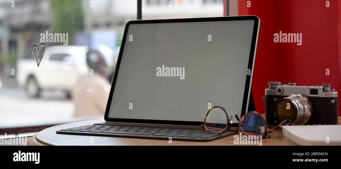 Un'area di lavoro portatile con un tablet, una fotocamera, occhiali e un notebook in legno sul bancone bar del bar Foto Stock