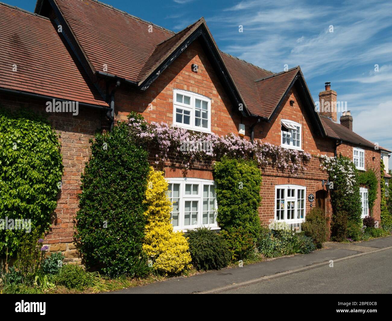 Grazioso, vecchio, inglese, mattoni rossi, cottage sul lato della strada in primavera con cielo blu e piante di arrampicata, Burton Lazars, Leicestershire, Inghilterra, Regno Unito Foto Stock