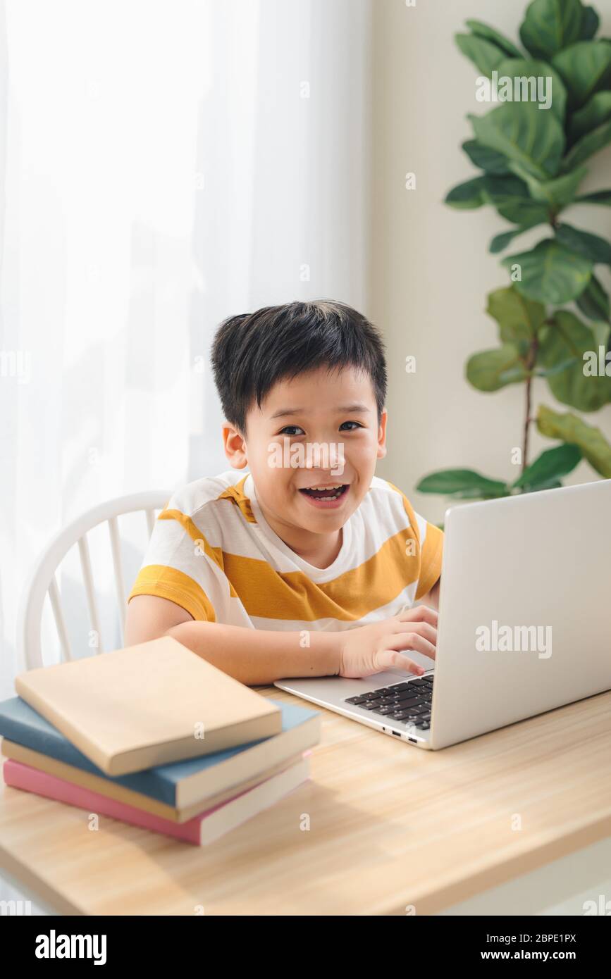 Asia presteen boy studia online su laptop con un volto sorridente e divertente a casa. Online Education e concetto di e-learning. Foto Stock