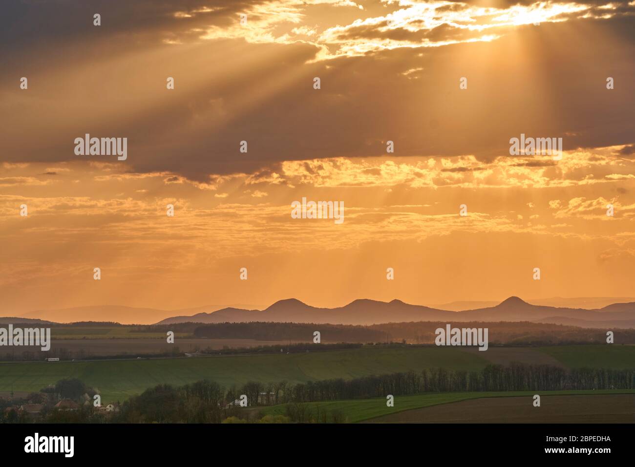 Tramonto si affaccia su un paesaggio mozzafiato con colline sullo sfondo e campi e prati in primo piano, durante il tramonto con nuvole arancioni Foto Stock