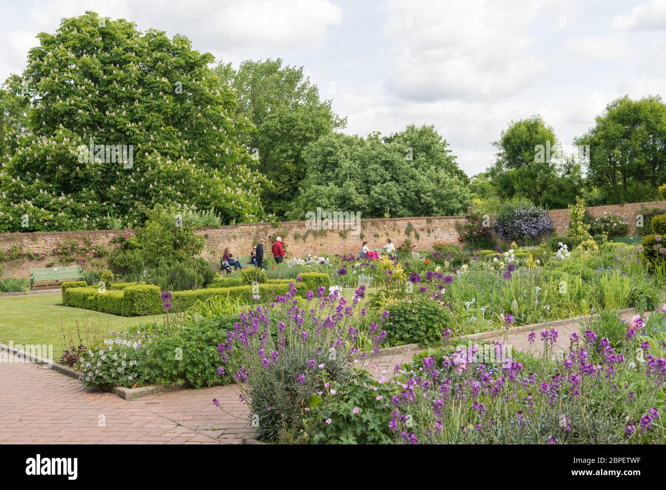 Le persone si rilassano nel giardino murato dell'Eastcote House Gardens durante una giornata soleggiata e calda in tarda primavera. Inghilterra, Regno Unito. Foto Stock