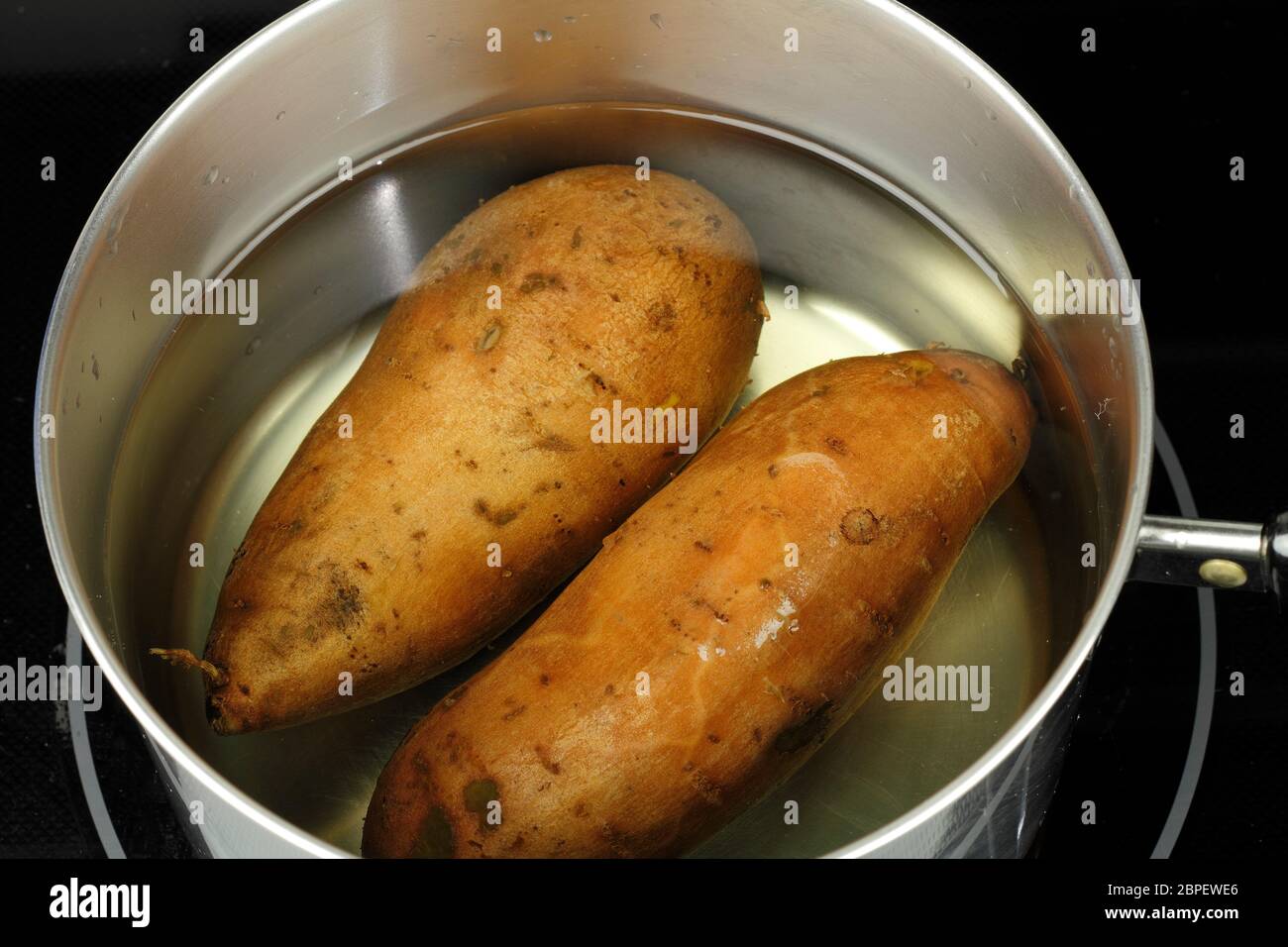 Preparare due patate dolci d'arancia, ipomea battatas, in una padella d'acqua pronta a bollire. Primo piano di due patate dolci intere non cotte in acqua in un de Foto Stock