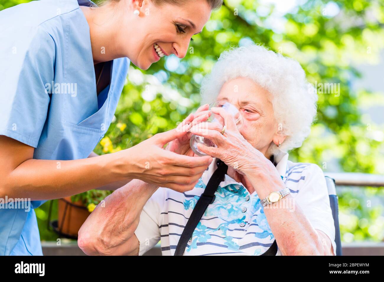 Infermiera geriatrica dando un bicchiere di acqua alla donna senior Foto Stock