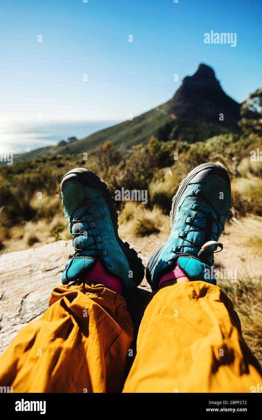 Piedi di una donna alpinista rilassante sulla cima della scogliera. Prospettiva personale di escursionista donna che riposa su sentiero di montagna. Foto Stock