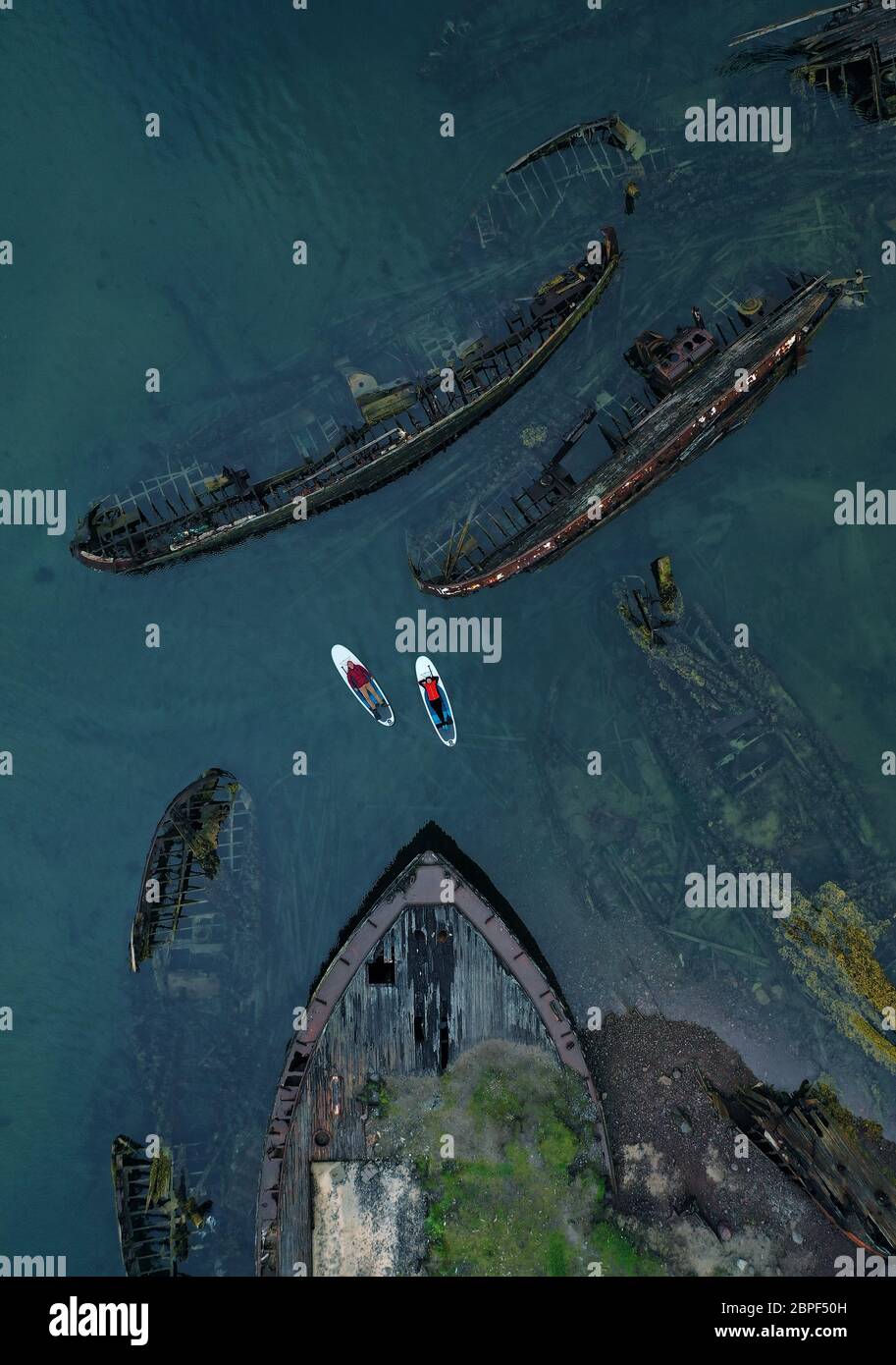 Uomo e donna sulle tavole SUP nel cimitero delle navi. Vista aerea. Teriberka, Penisola di Kola, Russia. Foto Stock