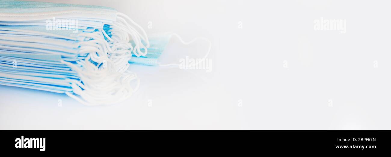 Pila di maschere chirurgiche monouso medico su sfondo bianco panoramico con spazio di copia, Covid-19 protezione banner web Foto Stock