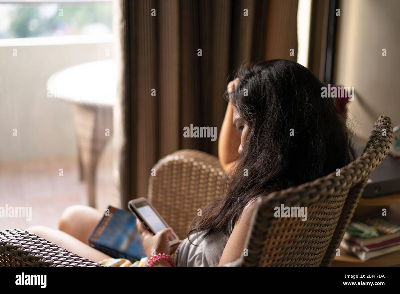 Immagine concettuale di noia o problemi di salute mentale come una donna seduta in una sedia fissa un telefono cellulare durante un periodo di quarantena nel COVID-19 Pandemic 2020 Foto Stock