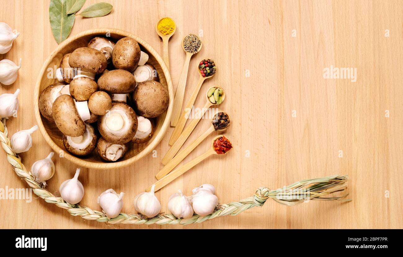 Funghi in piatto di legno, treccia di aglio, foglie di alloro, vari cucchiai con spezie diverse. Vista dall'alto. Foto Stock