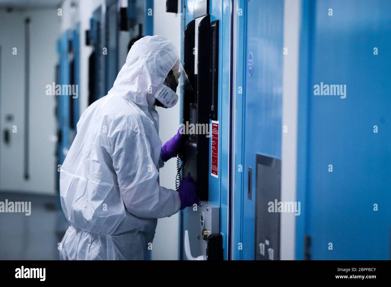 Un membro del team di custodia di PSNI Musgrave Street guarda attraverso una porta cellulare che indossa i DPI necessari per interagire con una persona sospetta detenuta da Covid-19 in un blocco di detenzione presso la stazione di Belfast. PA Media ha avuto il primo accesso esclusivo al blocco Covid-19 per assistere a come il Servizio di polizia dell'Irlanda del Nord (PSNI) si è adattato alle sfide della custodia in una pandemia. Foto Stock