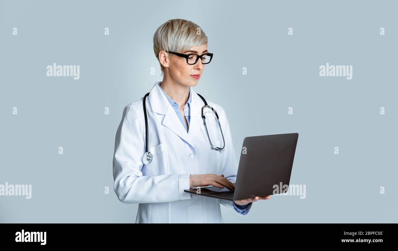 Concetto moderno di appuntamento medico. Donna medico in camice bianco e occhiali scrivere storia medica al portatile Foto Stock