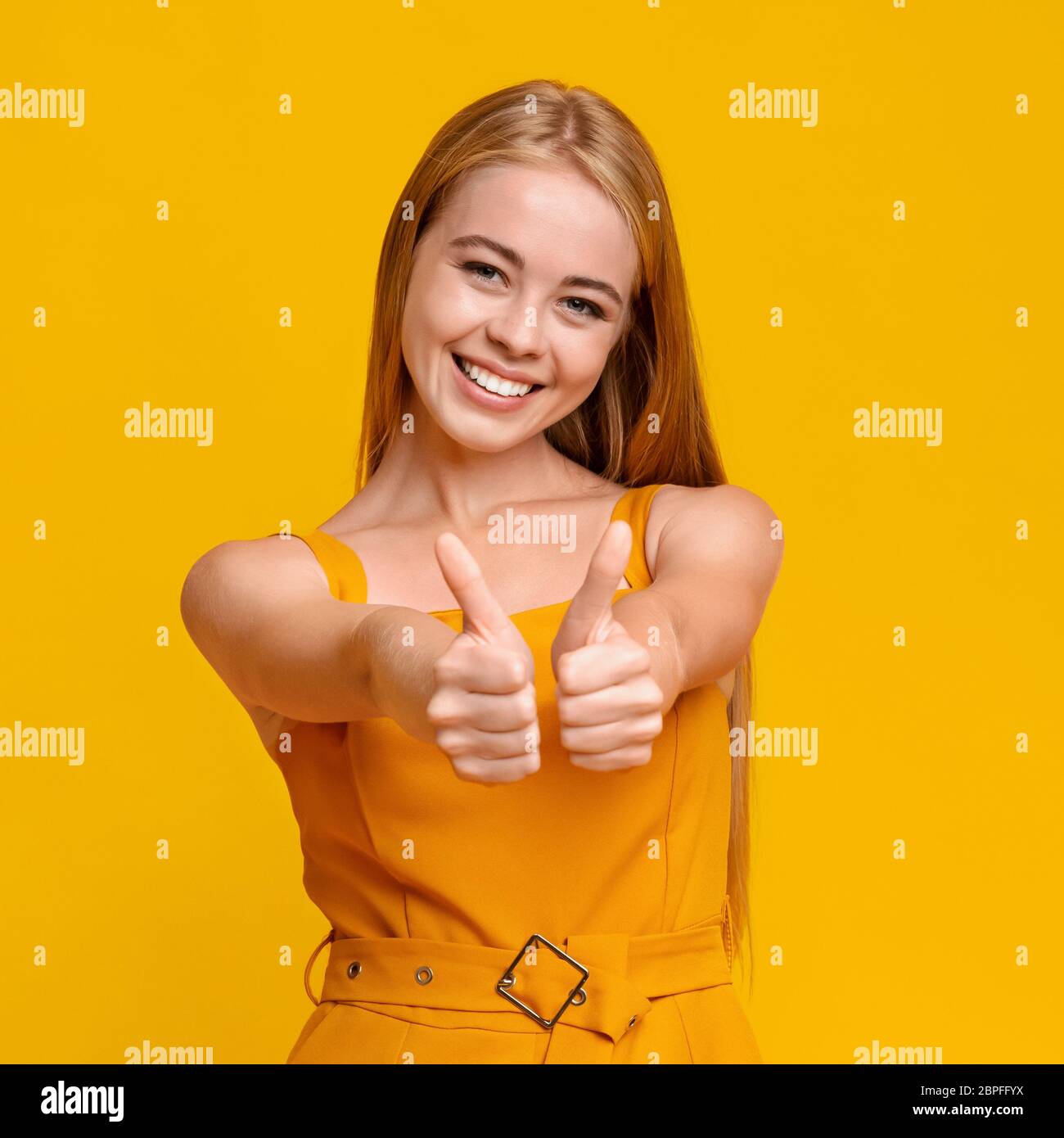 Gioiosa ragazza teen gesturing Thumbs Up a Camera su sfondo giallo Foto Stock