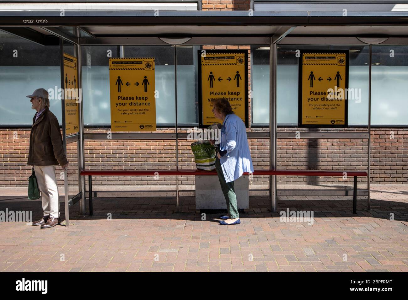 Una coppia anziana si trova a 2 metri di distanza in una fermata dell'autobus raccomandata dalle linee guida per l'allontanamento sociale della pandemia del coronavirus, Richmond upon Thames, UK Foto Stock