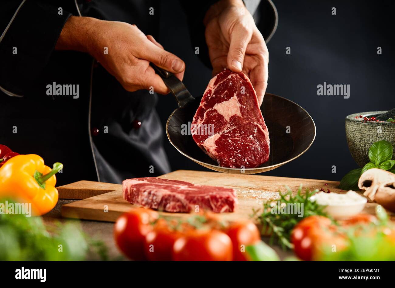 Lo Chef ponendo una bistecca di greggio in una padella per brasare o la cottura alla griglia con verdure fresche in primo piano Foto Stock