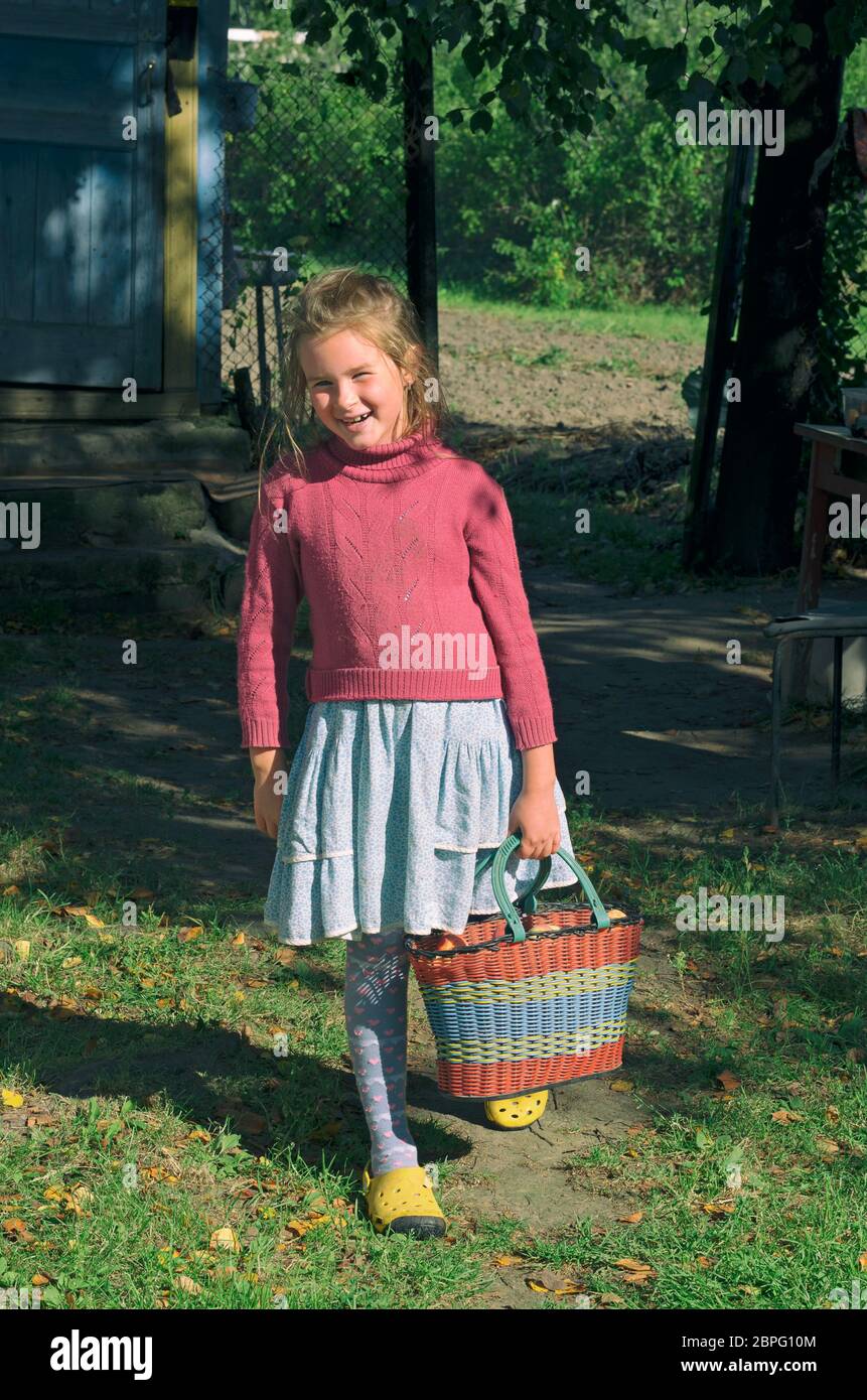 Country piccola ragazza in una posa rilassata con un sorriso e un cestino di mele in mano Foto Stock