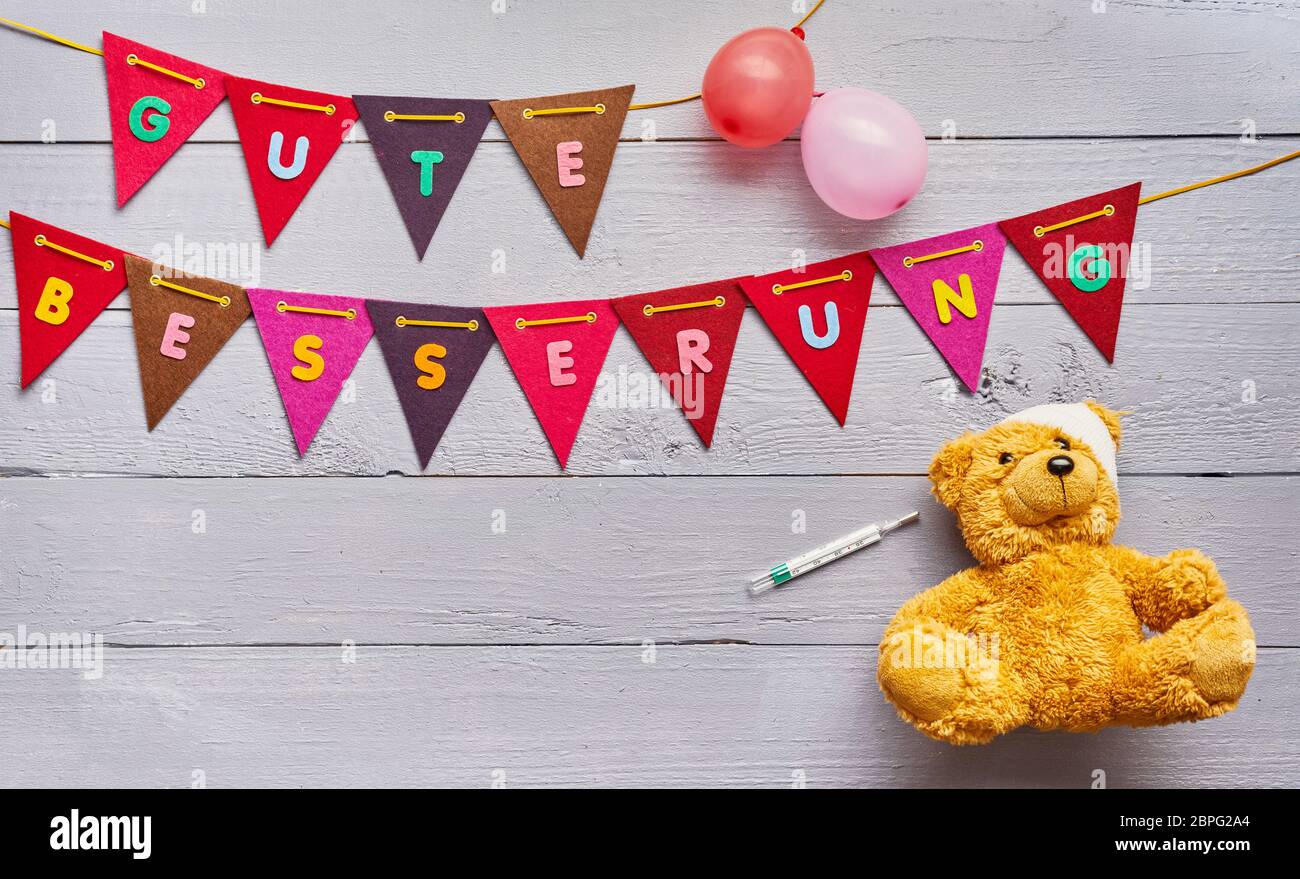 Gute Besserung - Get Well - concetto per bambini con colorati bunting con il testo al di sopra di un grazioso piccolo orsacchiotto con bendaggio e termometro in un paediatr Foto Stock