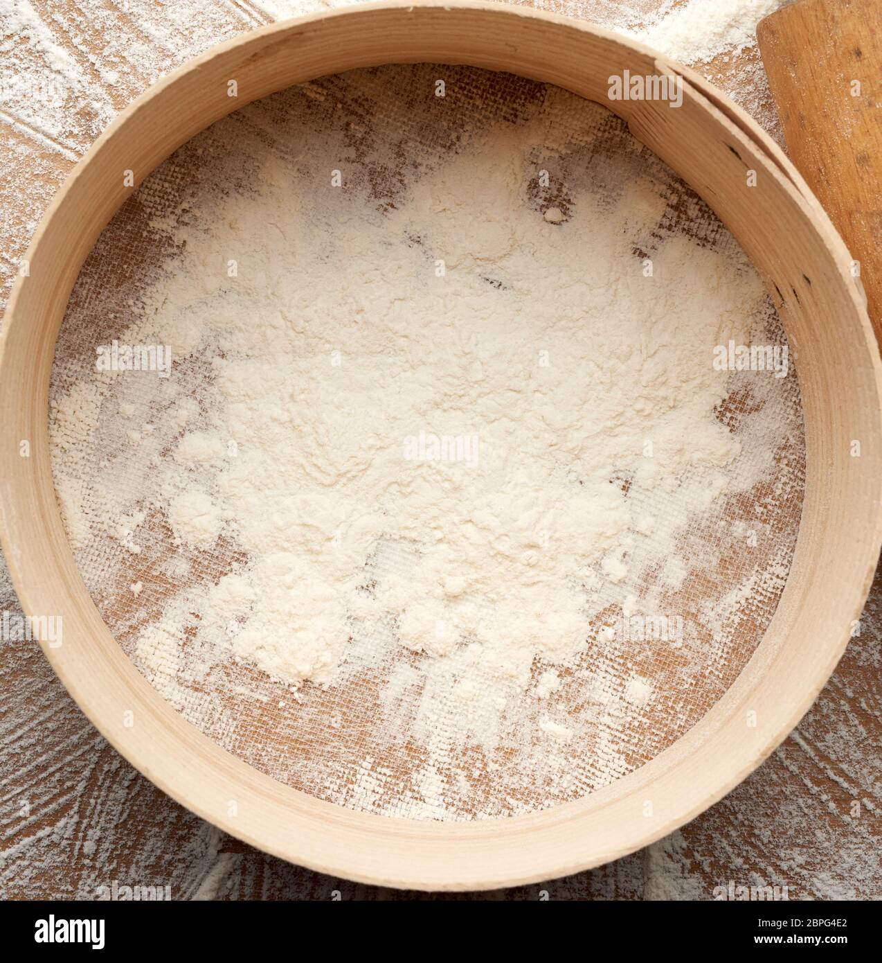 cospargere la farina di grano bianco e un setaccio di legno rotondo su un tavolo nero, vista dall'alto Foto Stock