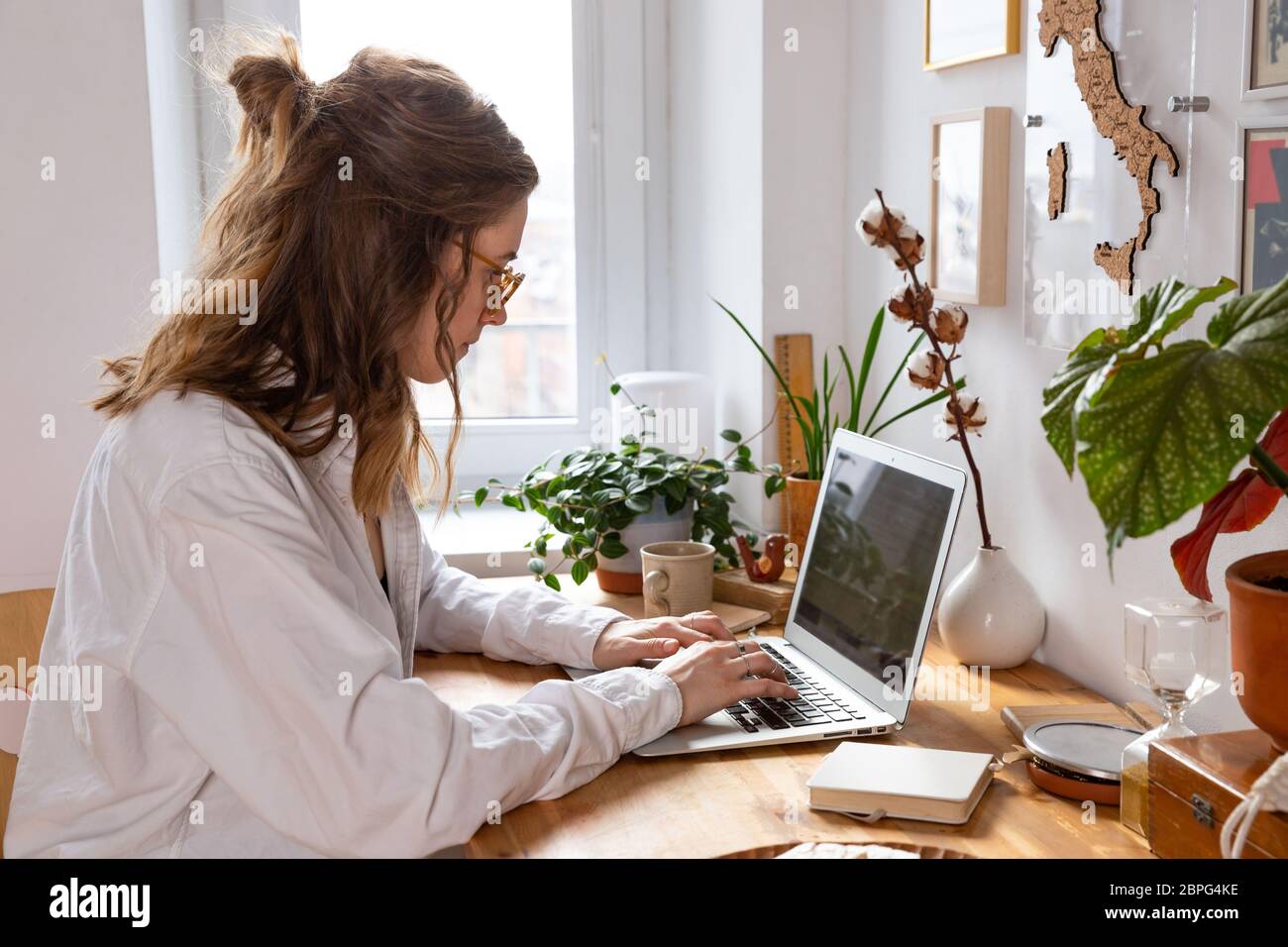 Giovane donna freelance/designer che lavora al computer da casa durante l'auto-isolamento a causa del coronavirus. Ambiente di lavoro accogliente circondato da piante Foto Stock