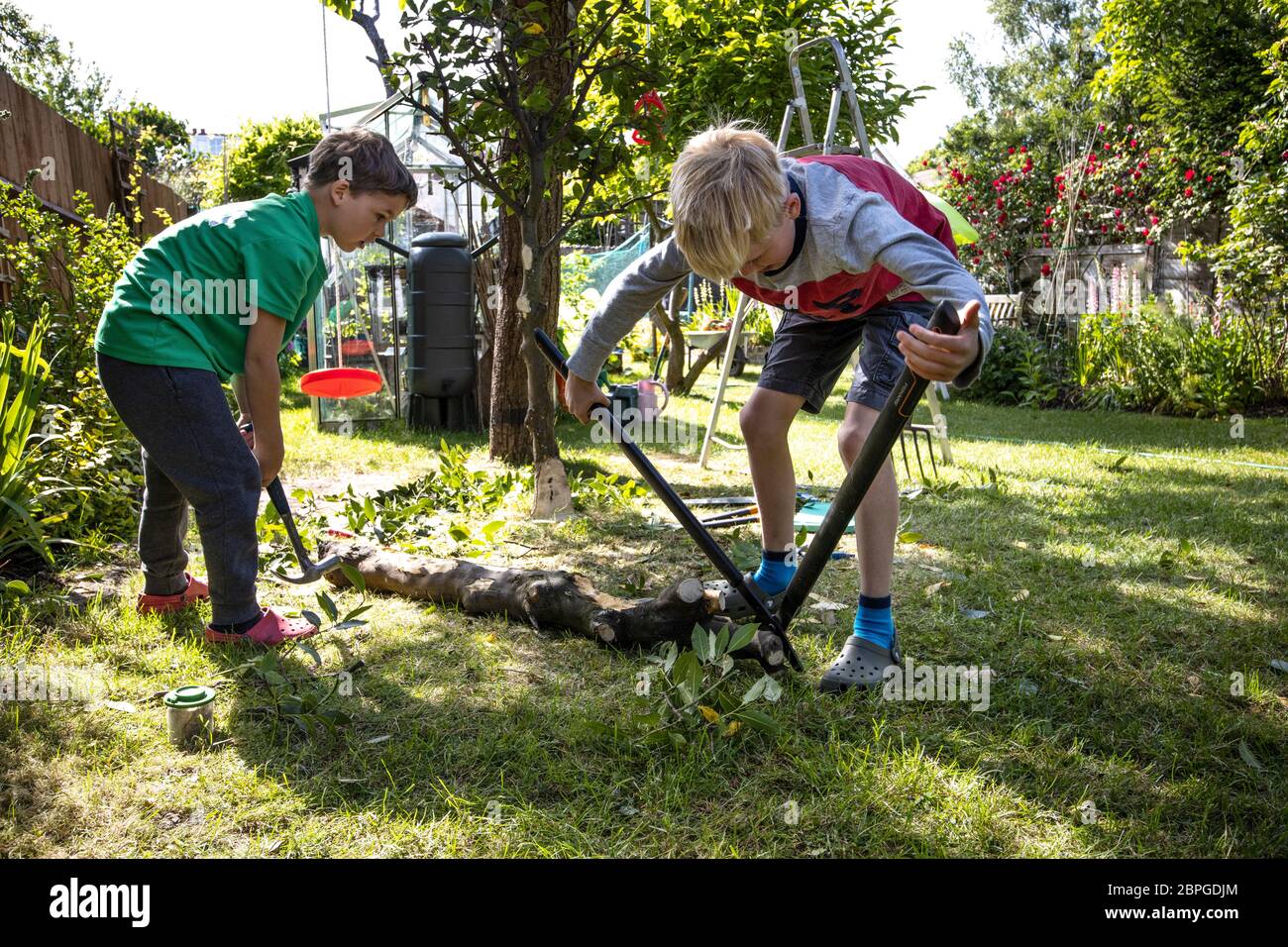 Giovani ragazzi che aiutano fuori in un giardino residenziale, Inghilterra, Regno Unito Foto Stock