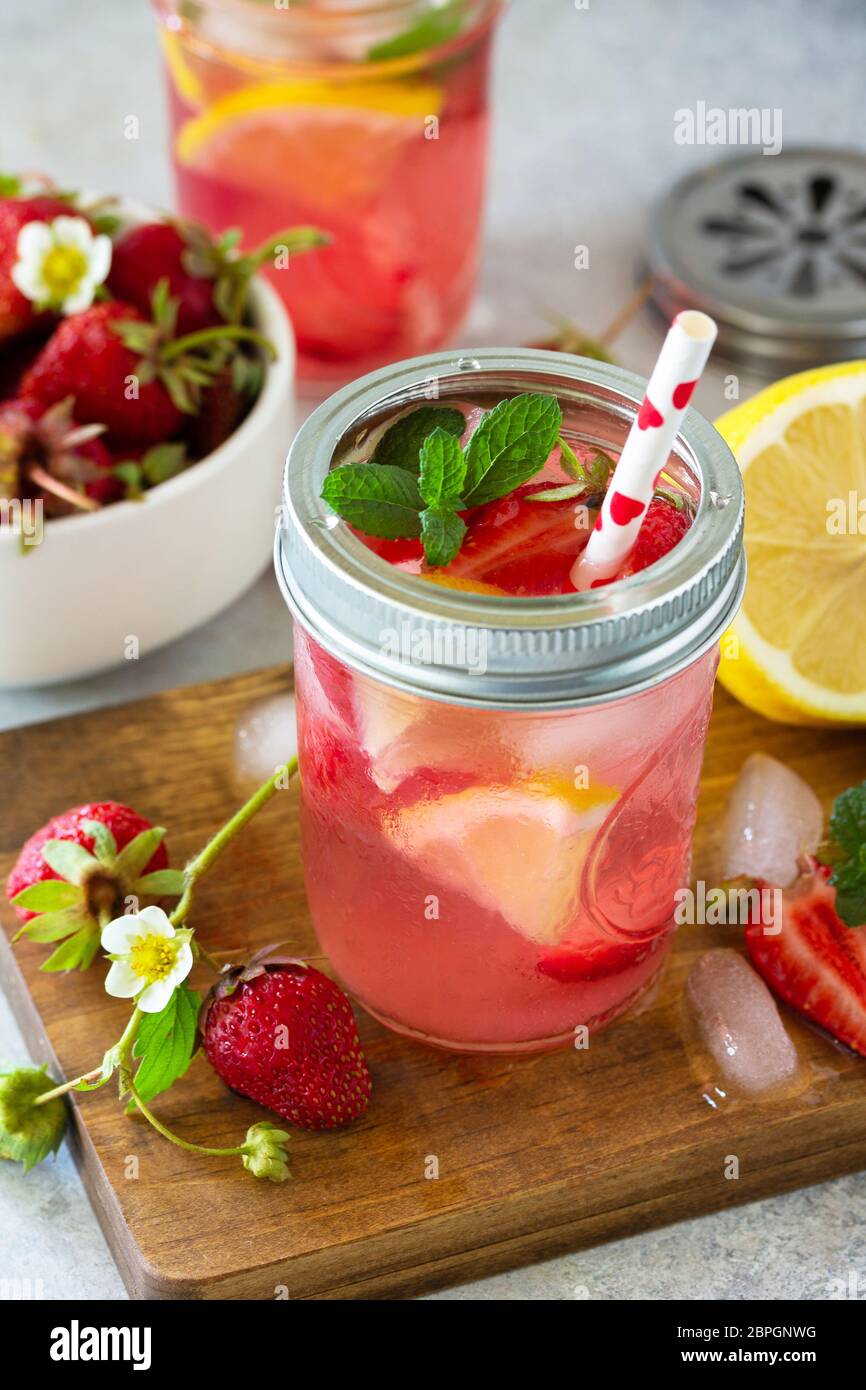 Bevanda estiva rinfrescante. Limonata con fragole fresche, ghiaccio e limoni su un piano di pietra leggero. Foto Stock
