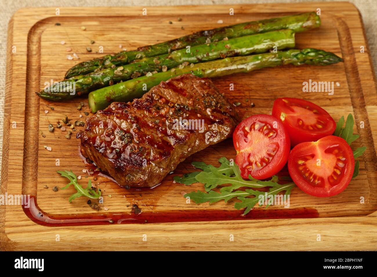 Chiudere una grigliata di carne di manzo arrosto di manzo con asparagi verdi e pomodori ciliegia sul tagliere di legno, ad alto angolo di visione Foto Stock