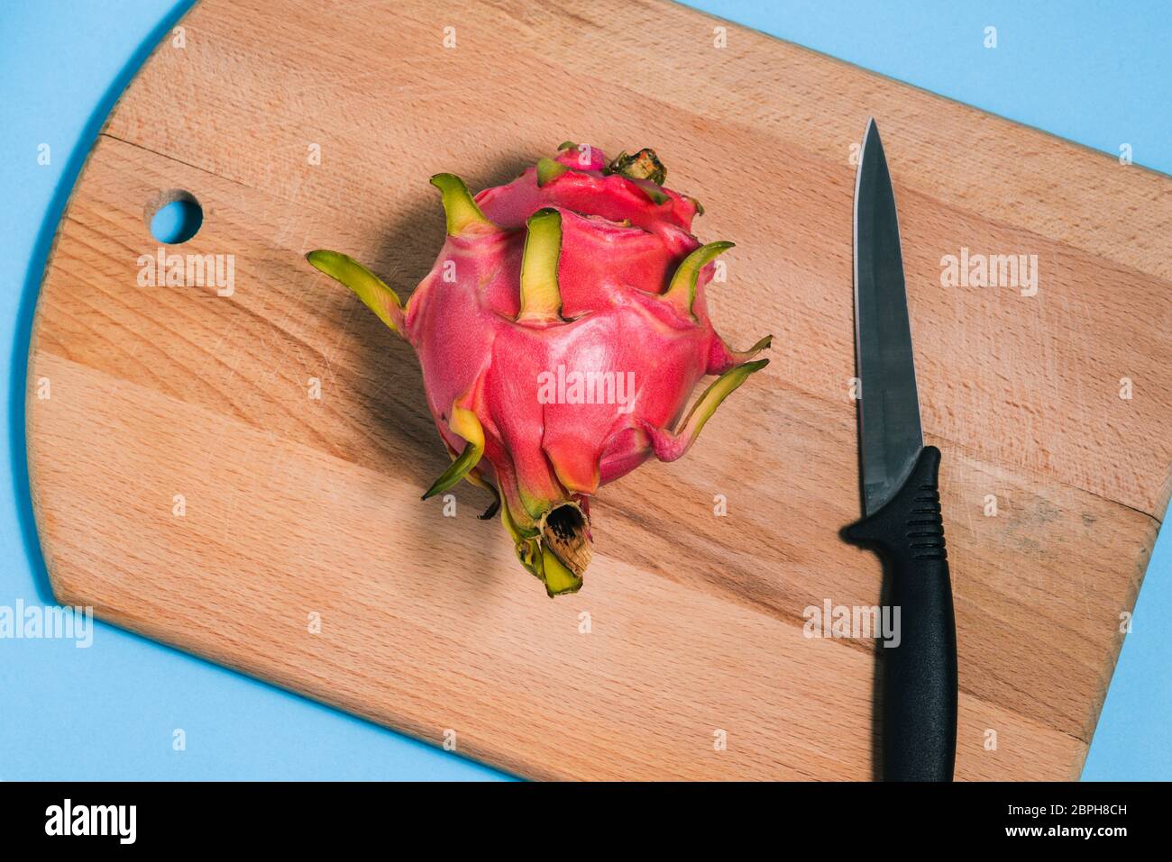 pitaya maturo e un coltello su una tagliere. Tagliare a metà il pitaya. Frutta di drago estate. Una vista dall'alto di un layout piatto. Foto Stock