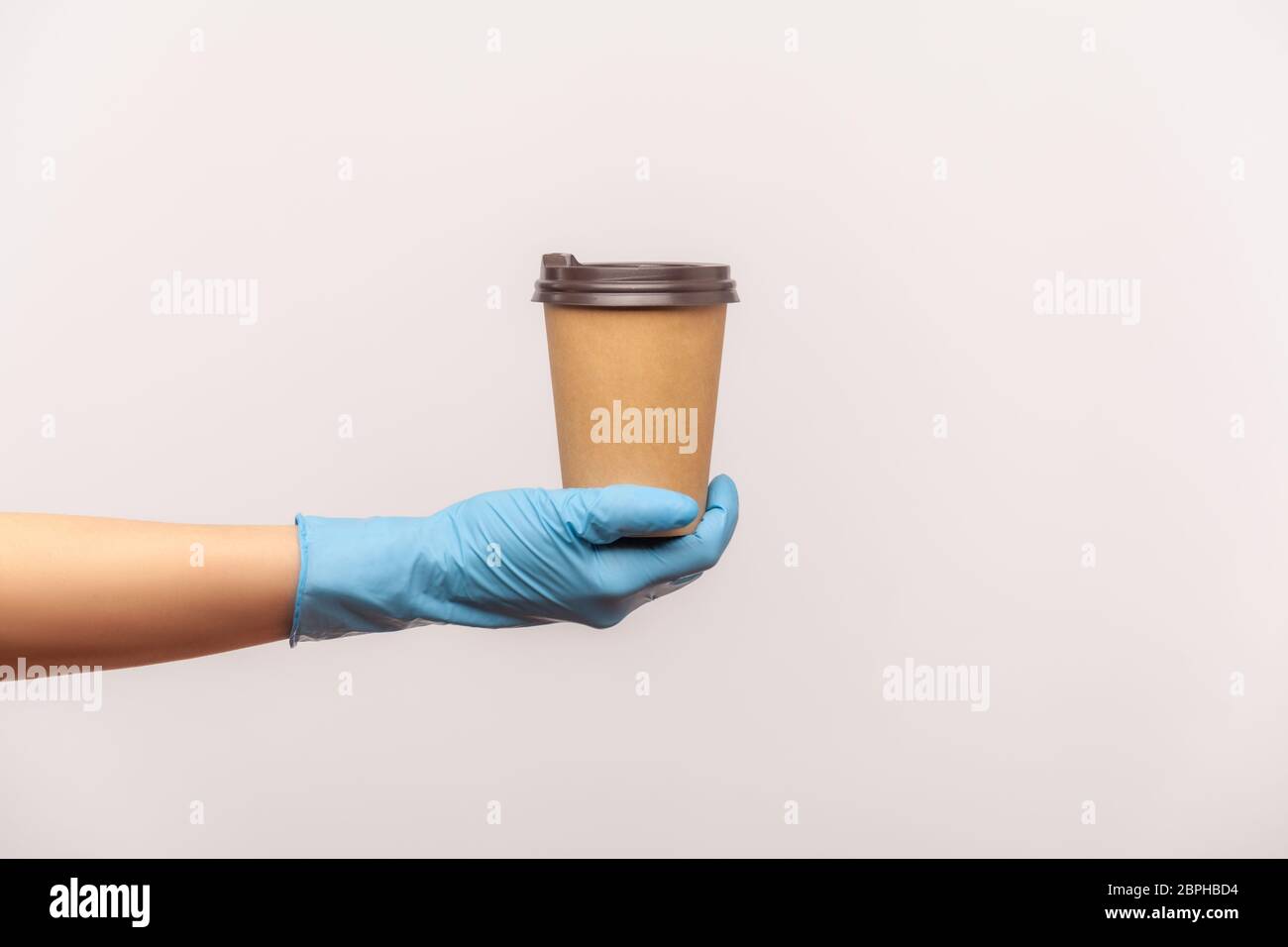Profilo Vista laterale primo piano della mano umana in guanti chirurgici blu che tengono in mano e mostrano una tazza di tazza da takeaway calda. Interno, studio shot, isolat Foto Stock