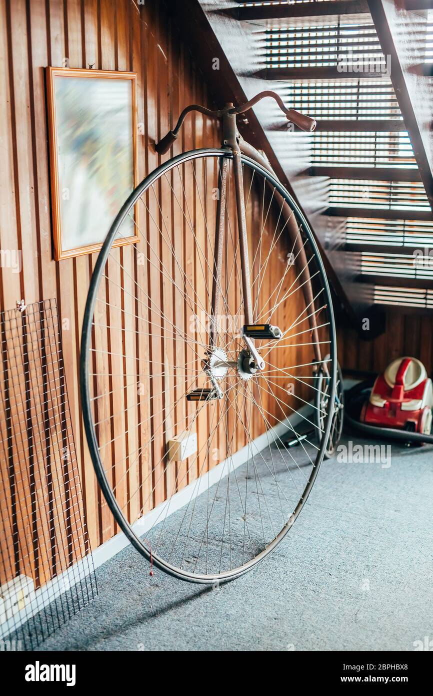 Bicicletta in stile antico con una ruota grande e una piccola sotto le scale in una casa. Foto Stock