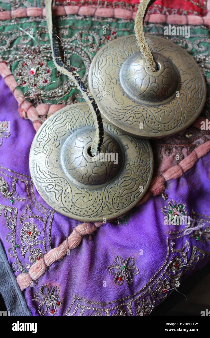 Tingsha (Ting-sha), campane di meditazione tibetane in primo piano, adagiandosi su un colorato cuscino indiano. Fuoco selettivo, copyspace sottostante. Foto Stock